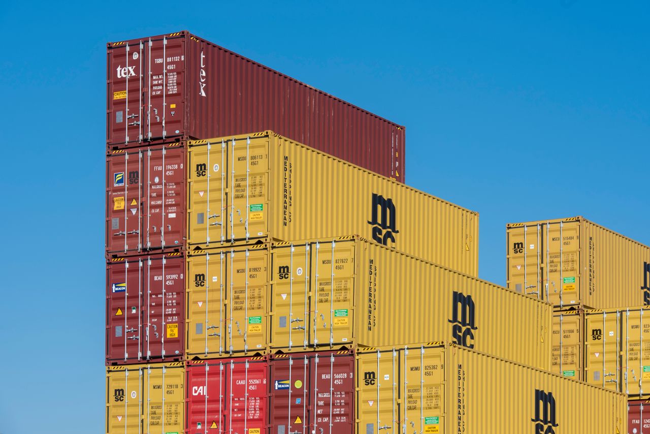 Colorful shipping containers stacked high under a clear blue sky, displaying industrial logistics.