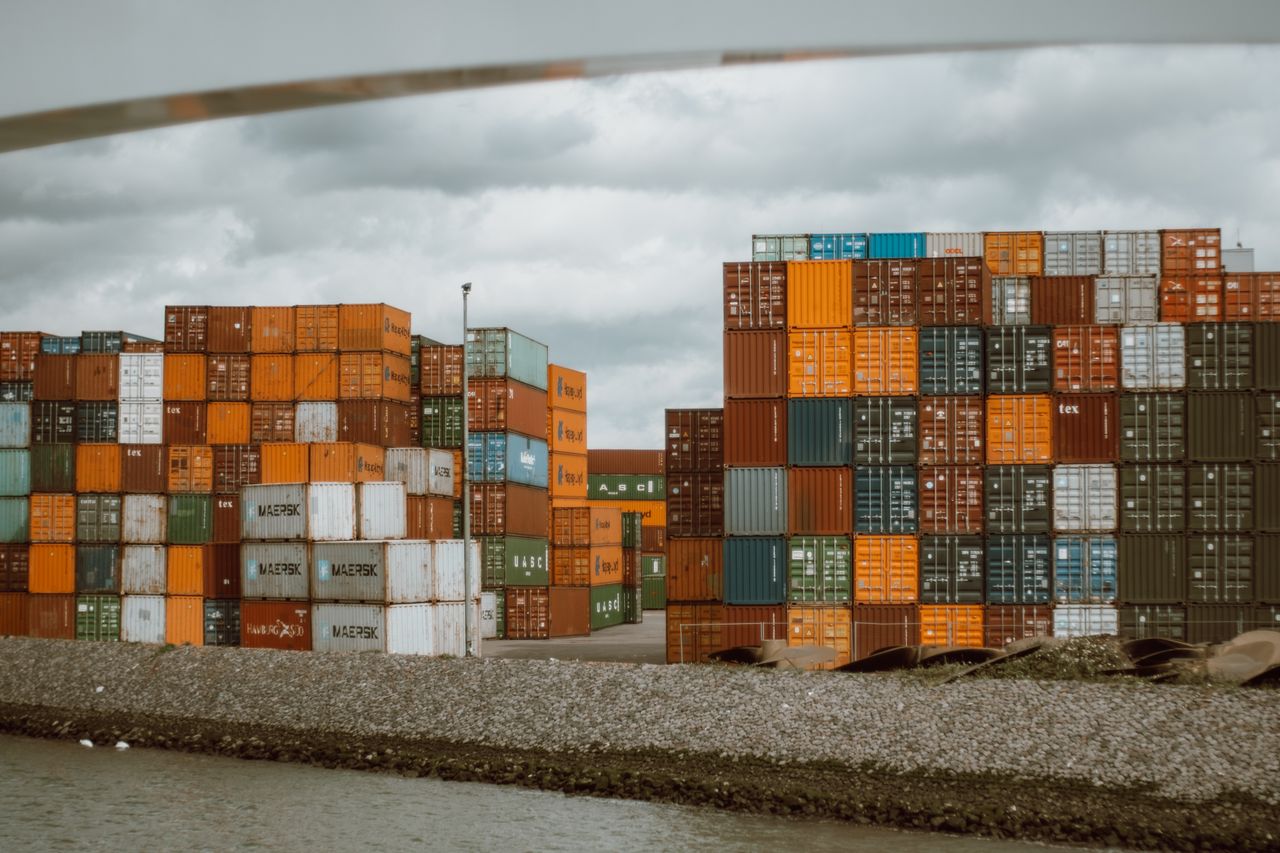 services-01 Colorful shipping containers stacked in Rotterdam harbor, under overcast skies.